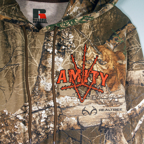 A camouflage embroidered hoodie by The Amity Affliction with "AMITY" in orange and barbed wire design, Russell Outdoors tag, Realtree logo on the front, shown on a plain light background.