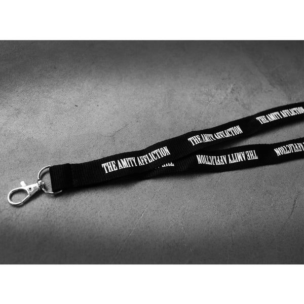 image of a black lanyard laid flat on a concrete floor. white text repeating around that says the amity affliction